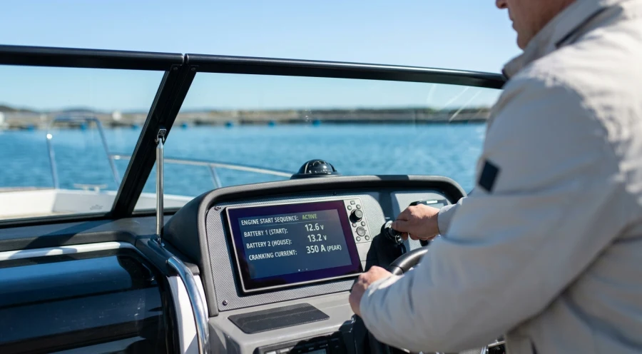 A modern marine multifunction display on a boat dashboard shows real-time battery voltage and current data during an engine cranking event.